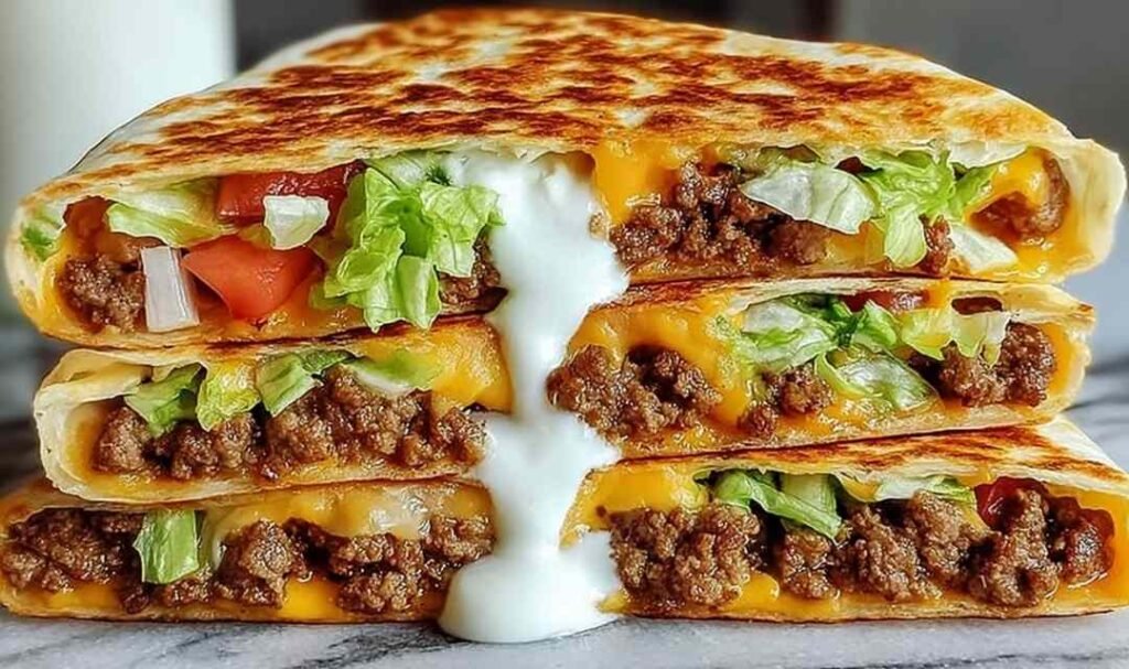 Keto crunchwrap cut in half showing seasoned ground beef, homemade cheese sauce, sour cream, lettuce, and tomato inside a crispy golden low-carb tortilla
