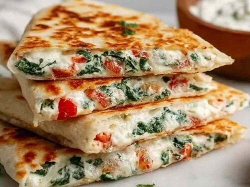 Cheesy Mediterranean quesadilla sliced into triangles on a white plate served with tzatziki dipping sauce