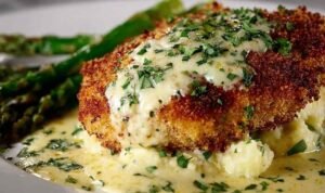 Parmesan crusted chicken cutlets topped with creamy garlic sauce and fresh parsley on a white dinner plate
