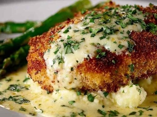 Parmesan crusted chicken cutlets topped with creamy garlic sauce and fresh parsley on a white dinner plate