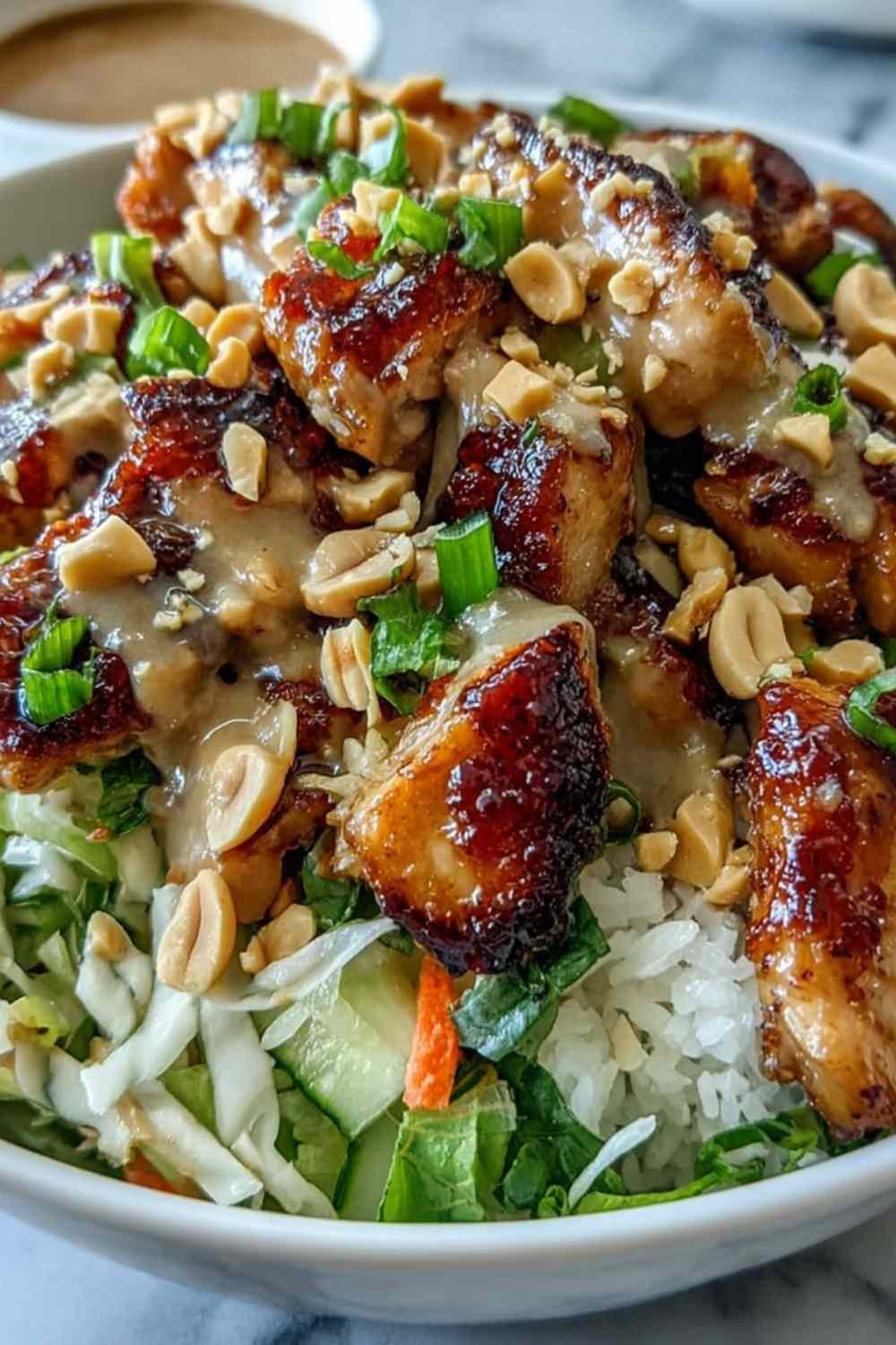 Peanut Chicken Protein Bowl with coconut jasmine rice, sauteed chicken, red cabbage, shredded carrots, and creamy Thai peanut sauce drizzled on top with lime wedge