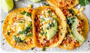 Shredded Chipotle Chicken Tacos Shredded chipotle chicken tacos topped with corn, avocado, cilantro, and cotija cheese on corn tortillas