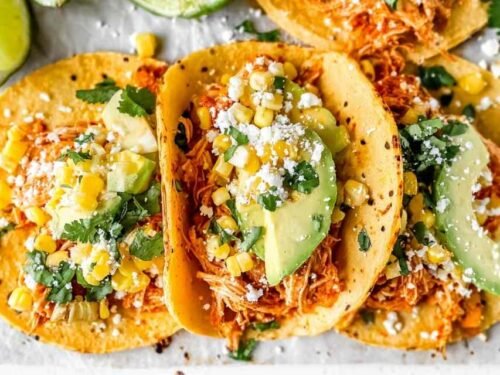 Shredded chipotle chicken tacos topped with corn, avocado, cilantro, and cotija cheese on corn tortillas