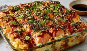 Spicy salmon sushi bake in a casserole dish topped with avocado, cucumber, green onions, and drizzled Kewpie mayo