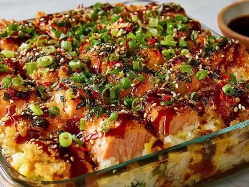 Spicy salmon sushi bake in a casserole dish topped with avocado, cucumber, green onions, and drizzled Kewpie mayo