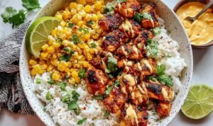 Street corn chicken rice bowl with charred corn, sliced grilled chicken, black beans, cotija cheese, and lime crema in a white bowl