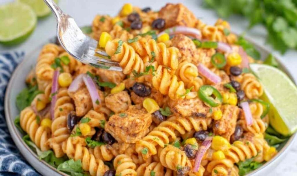 Zesty chicken enchilada pasta salad in a large white bowl with rotini, seasoned chicken, black beans, corn, and cilantro