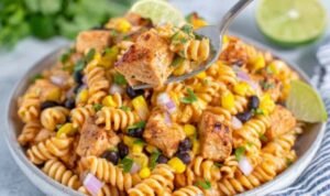 Zesty chicken enchilada pasta salad in a large white bowl with rotini, seasoned chicken, black beans, corn, and cilantro